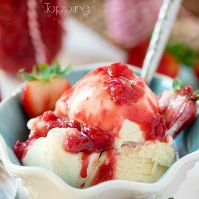 A bowl of vanilla ice cream with strawberry topping on top.