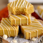 Pumpkin Fudge bars stacked on top of a decorative log with white chocolate pieces spread out.