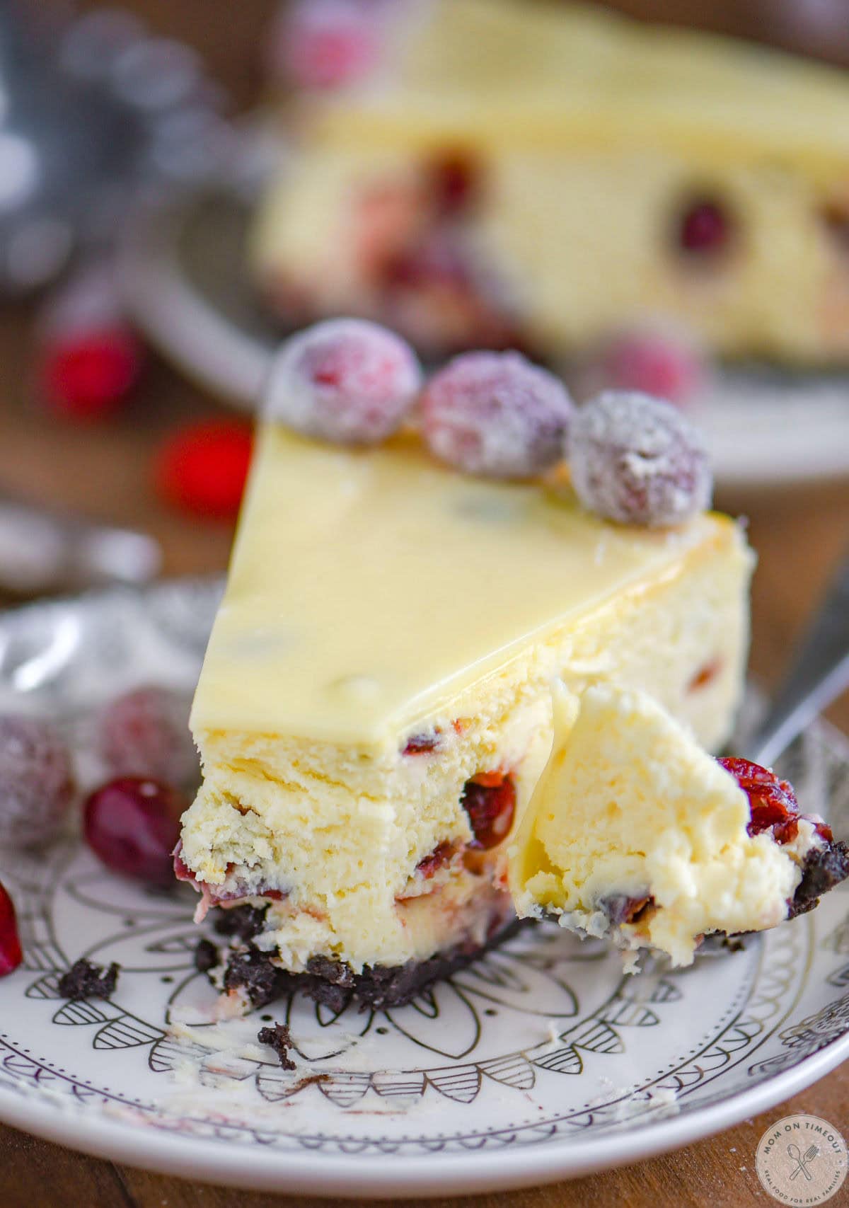 Piece of white chocolate cheesecake on round white dessert plate with bite cut off the end.