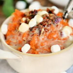 mashed sweet potatoes topped with marshmallows and pecans in beige bowl