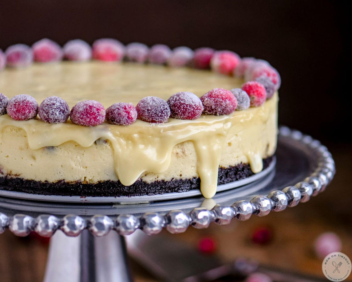 Wide shot of cheesecake with sugared cranberries on silver cake stand.