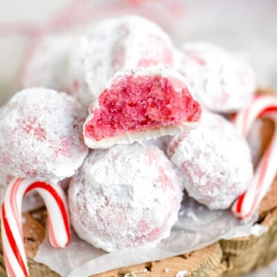 peppermint snowball cookie with bite taken sitting on top of a pile of more cookies with two candy canes on either side