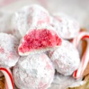 peppermint snowball cookie with bite taken sitting on top of a pile of more cookies with two candy canes on either siide