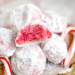 peppermint snowball cookie with bite taken sitting on top of a pile of more cookies with two candy canes on either siide