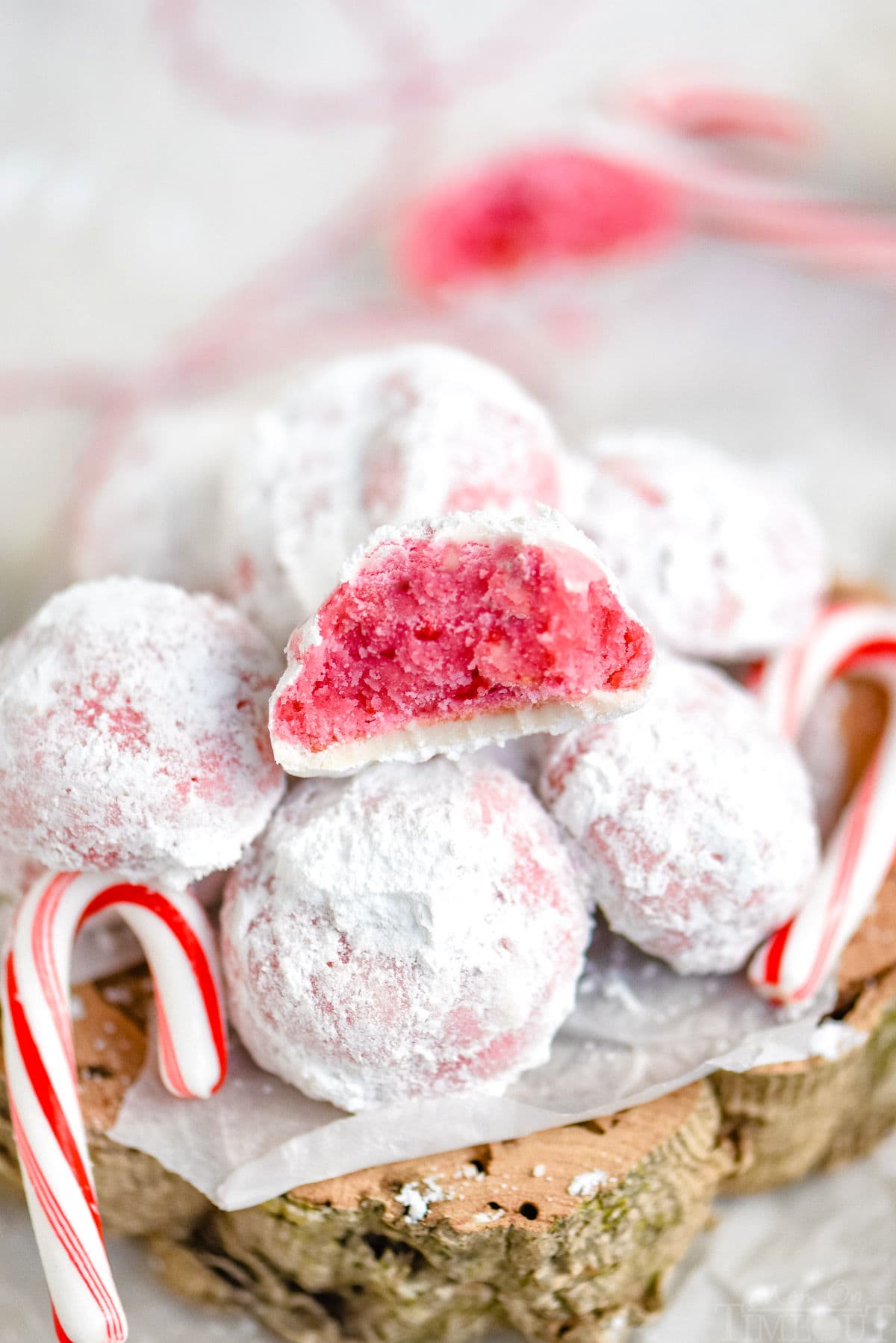 peppermint snowball cookie with bite taken sitting on top of a pile of more cookies with two candy canes on either side