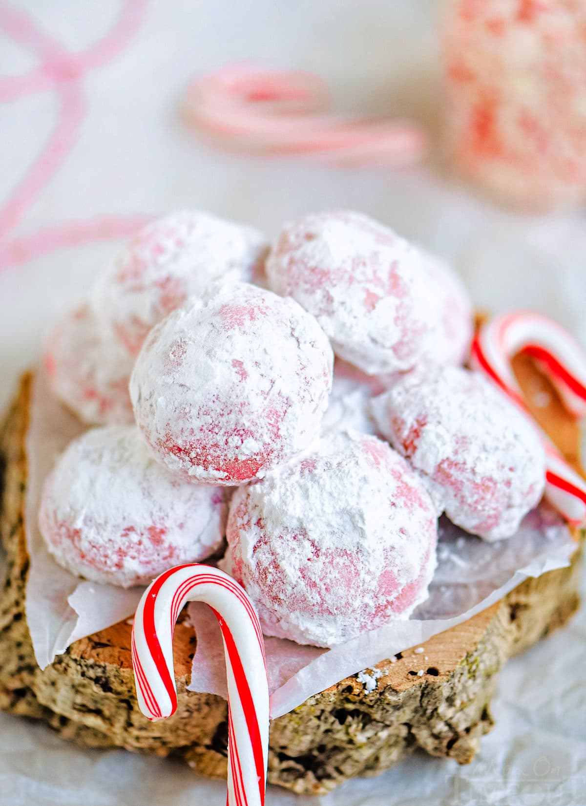 snowball cookies rolled in powdered sugar and piled on small wood block with mini candy canes scattered around it