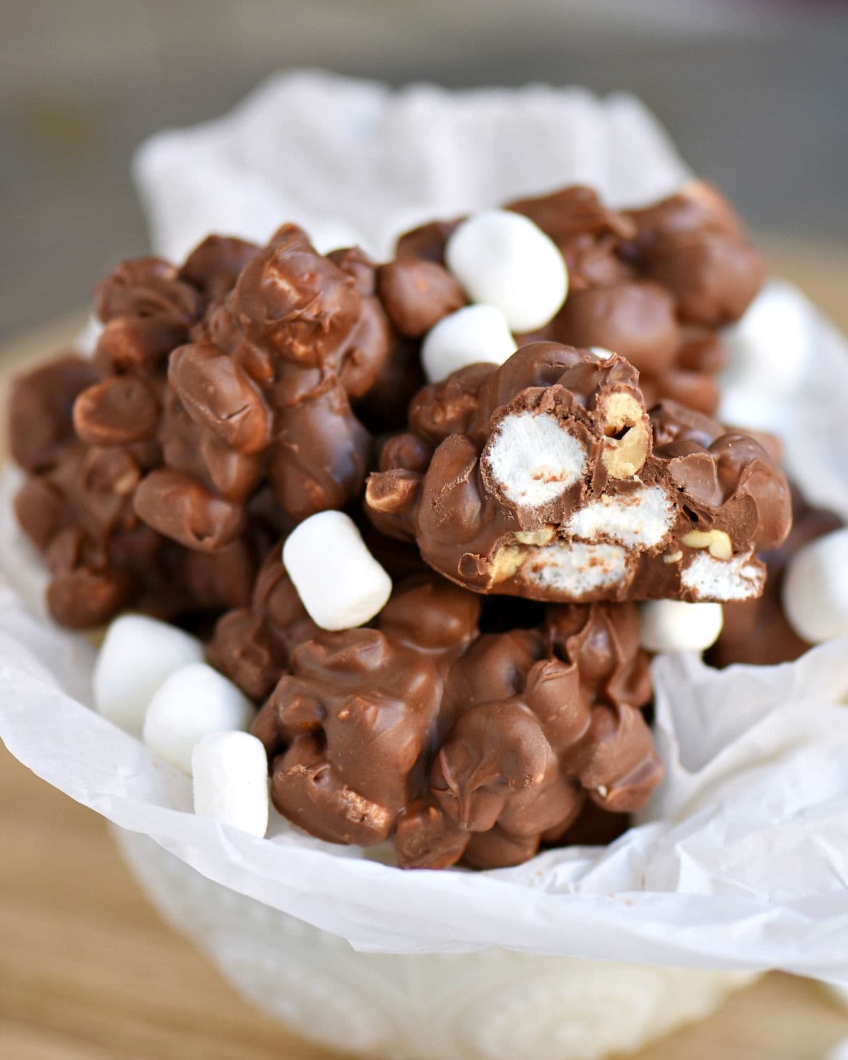 white bowl full of rocky road peanut clusters with one cut in half. marhsmallows are scattered on top.