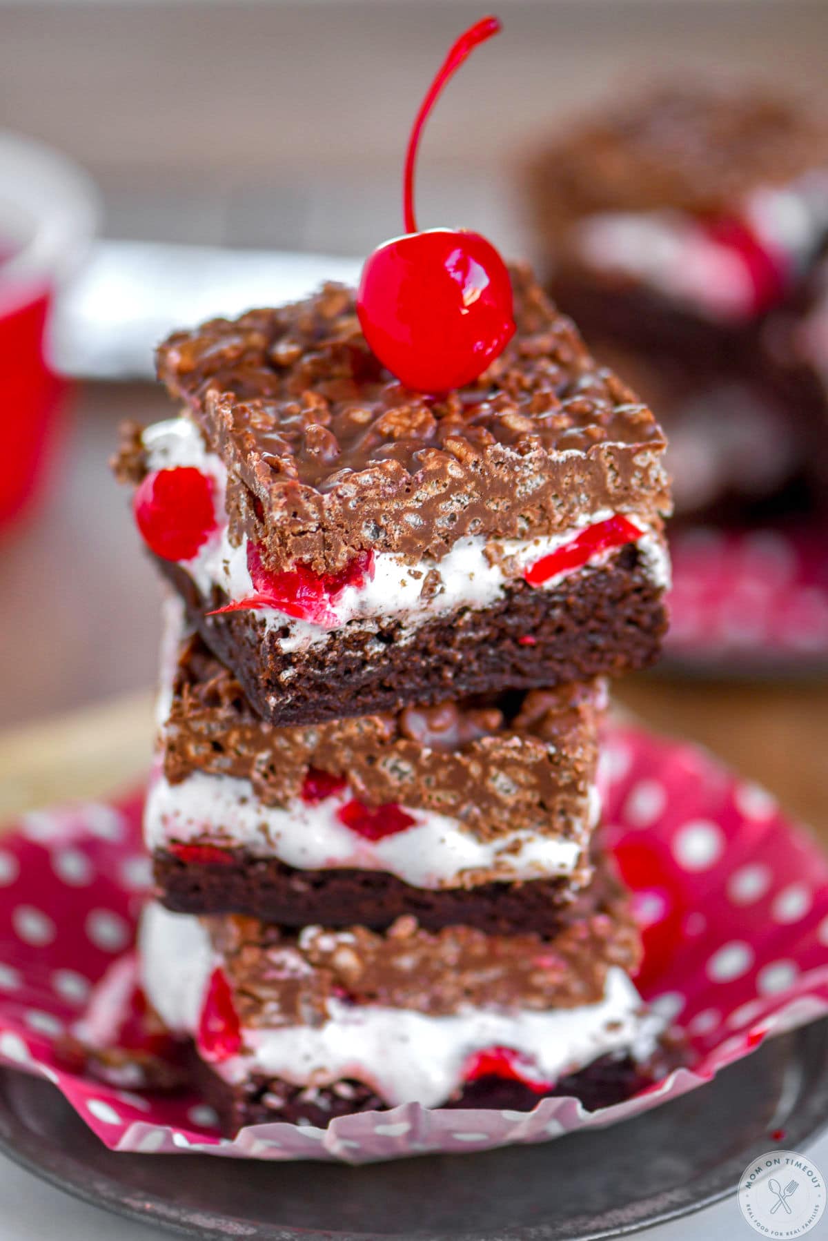 Stack of three cherry brownie dream bars on a metal plate with a maraschino cherry on top.