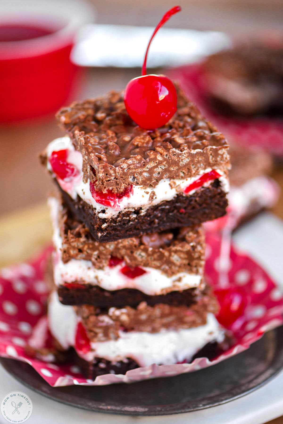 Stack of three cherry brownie dream bars on a metal plate with a maraschino cherry on top.