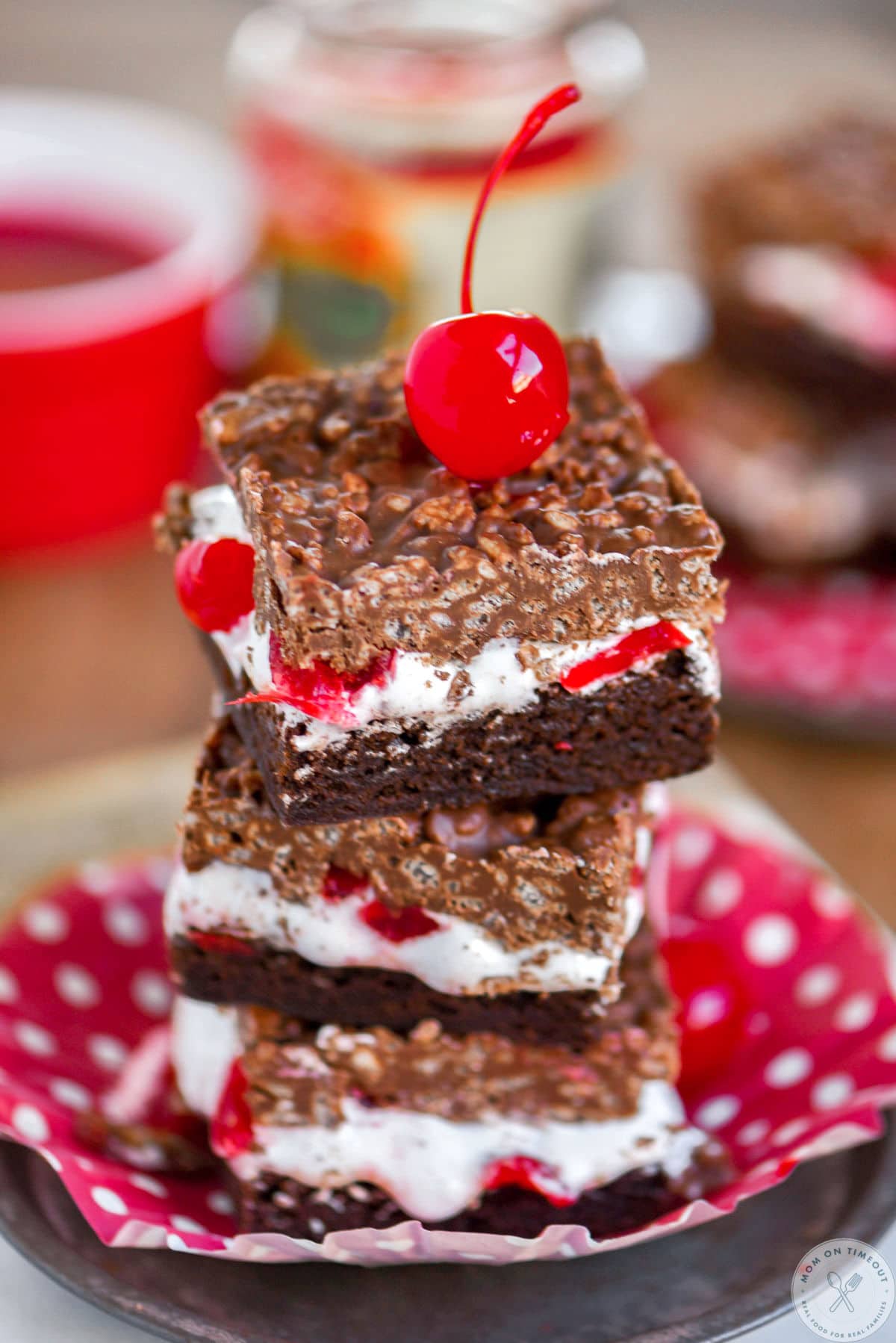 Stack of three cherry brownie dream bars on a metal plate with a maraschino cherry on top.
