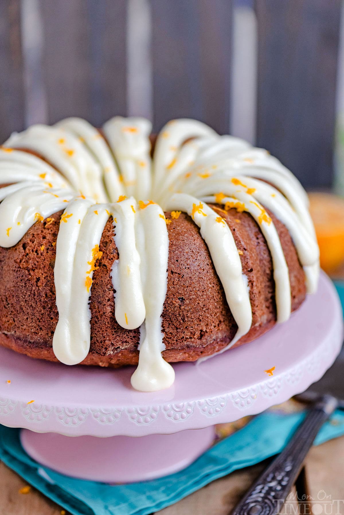 hummingbird cake on pink cake stand with cream cheese frosting drizzled over the top.