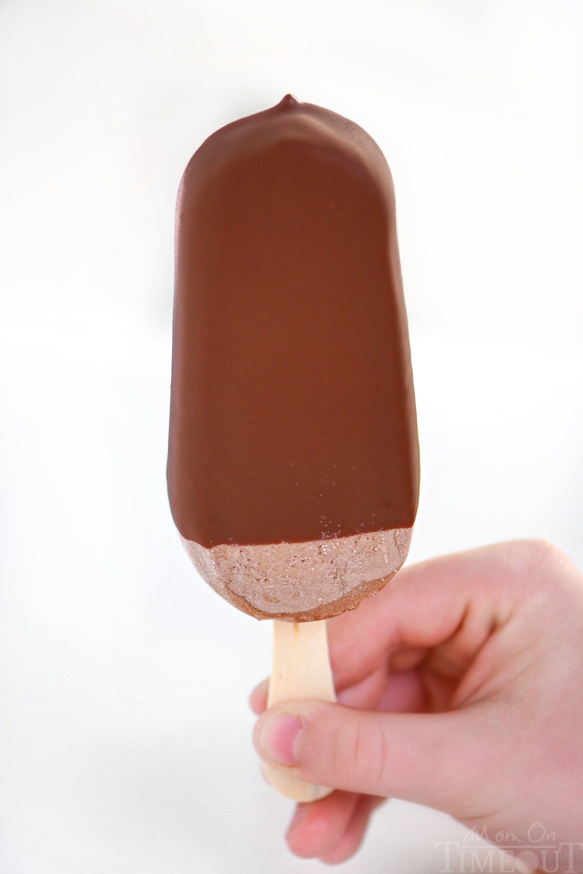 Child's hand holding up a magic shell dipped fudge pop.