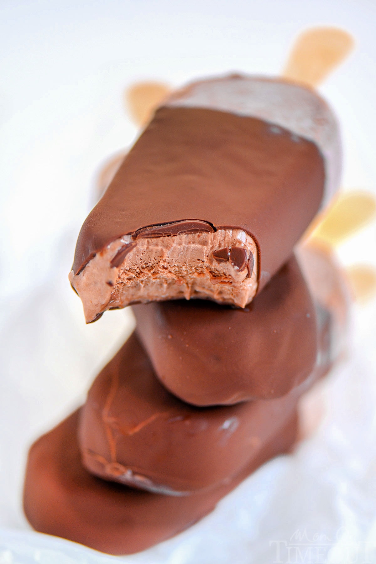 Four fudge bars that have been dipped in magic shell stacked on each other with popsicle sticks out the back.