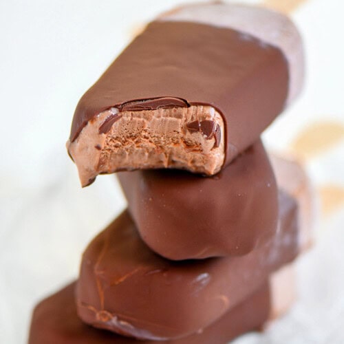 Four fudge bars that have been dipped in magic shell stacked on each other with popsicle sticks out the back.
