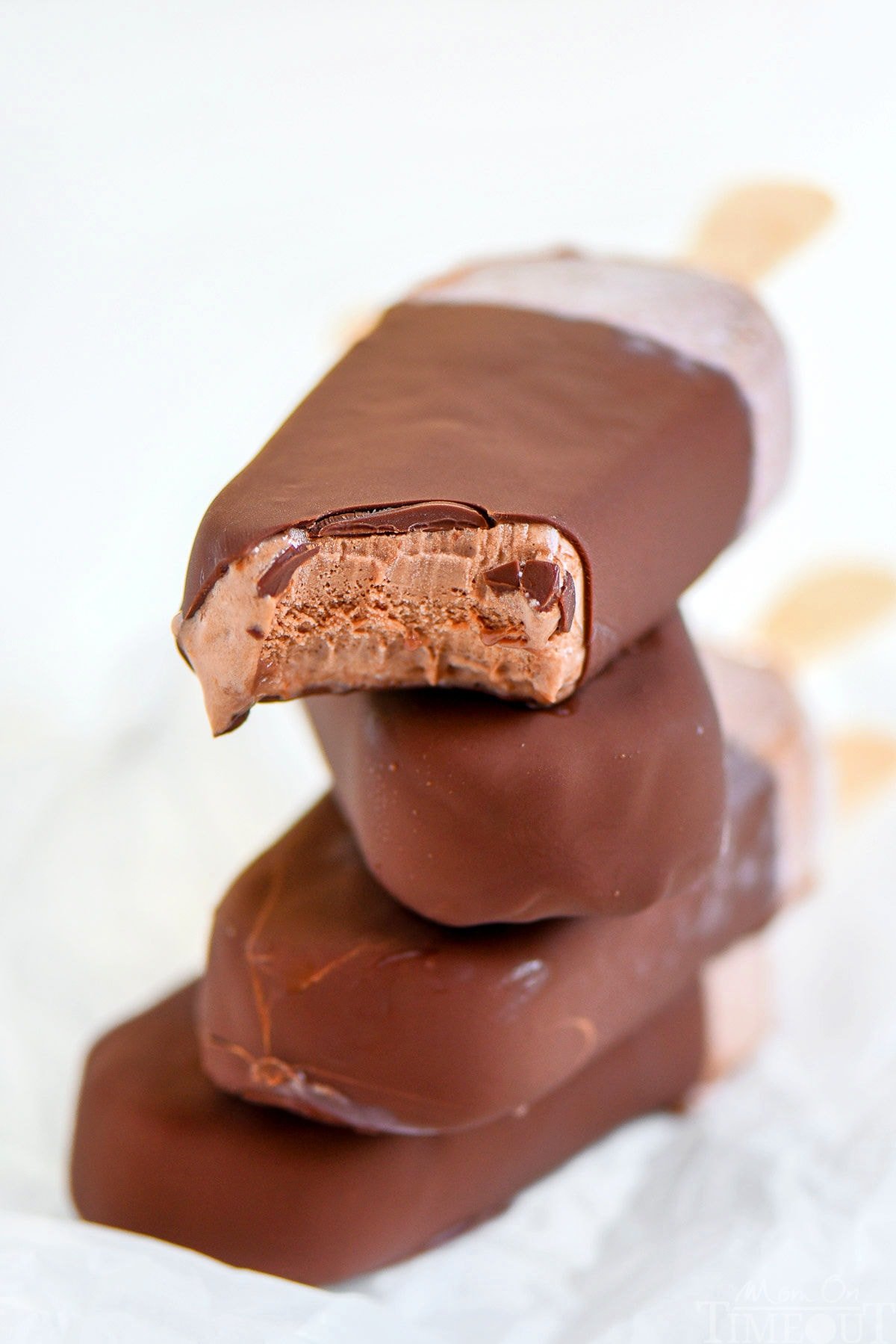 Four fudge bars that have been dipped in magic shell stacked on each other with popsicle sticks out the back.