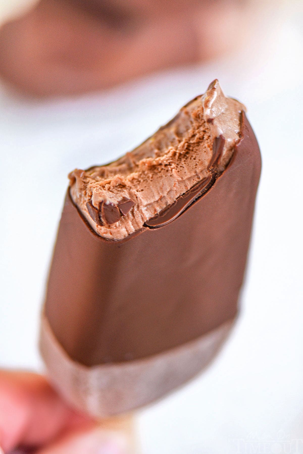 Magic shell coated fudge bar with bite taken out of it being held up.