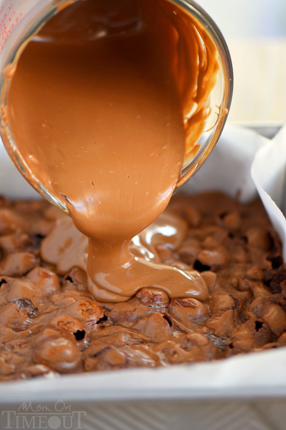 chocolate frosting being poured over baked brownies