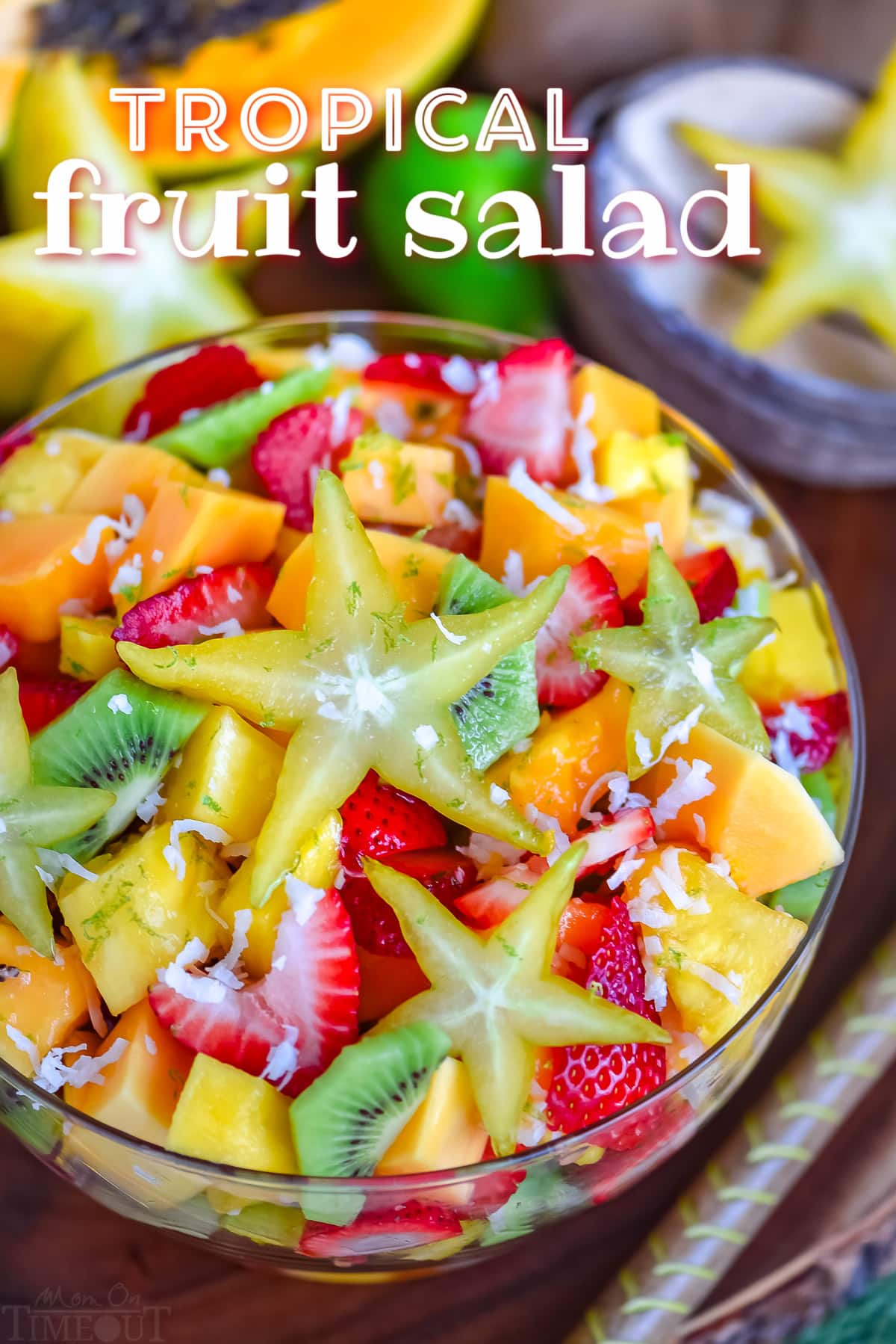 fruit salad made with tropical fruits like kiwi, papaya, mango and more in a large glass bowl. title overlay at top of image.
