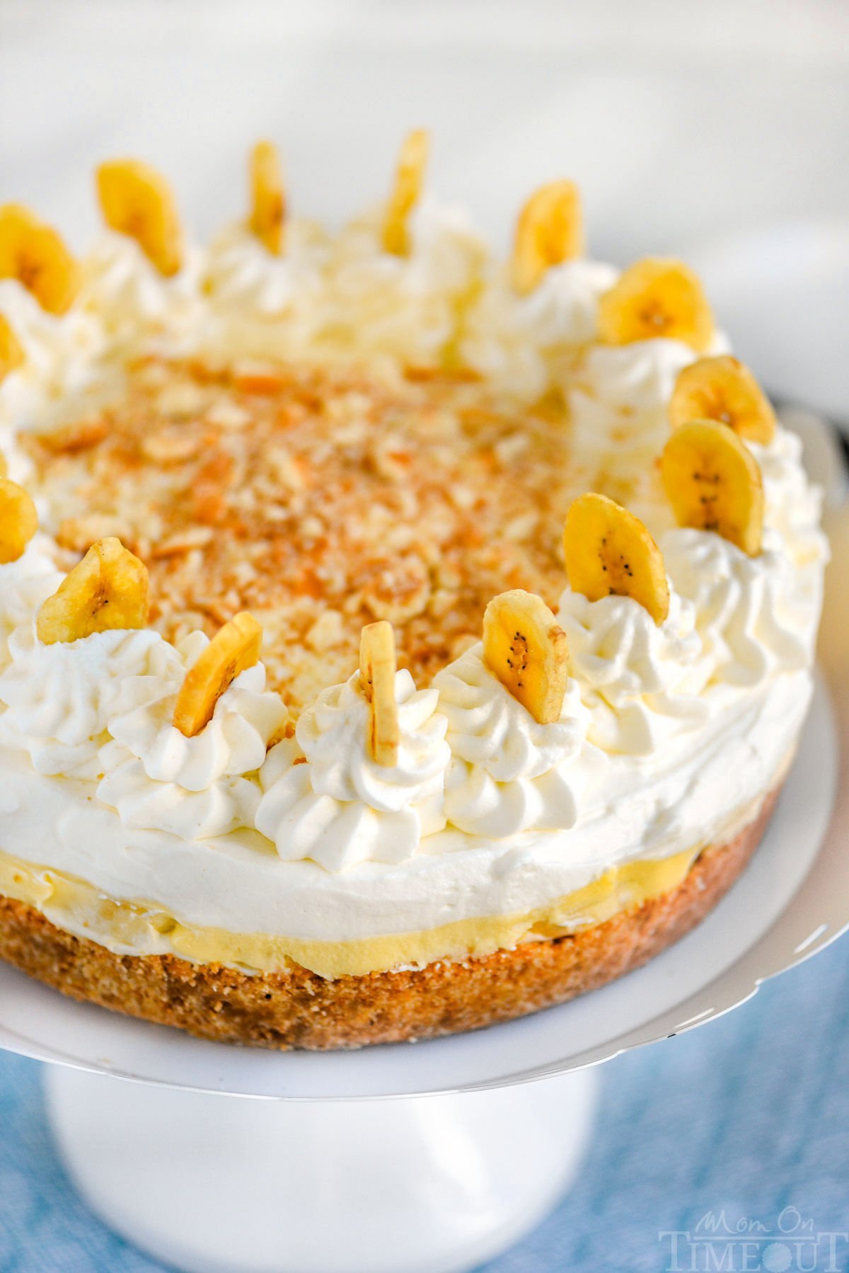Top down angled view of the garnish on the banana cream cheesecake that includes banana chips, fresh whipped cream and cookie crumble.