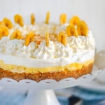 Whole no bake banana pudding cheesecake on white metal stand ready to be served.
