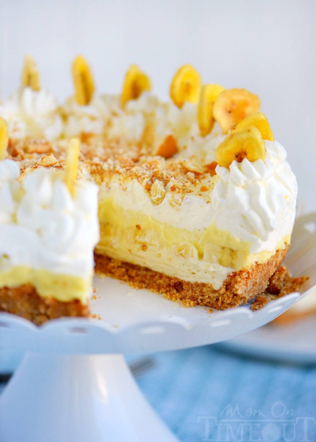 whole Banana Cream Pudding Cheesecake on white cake stand with one slice removed