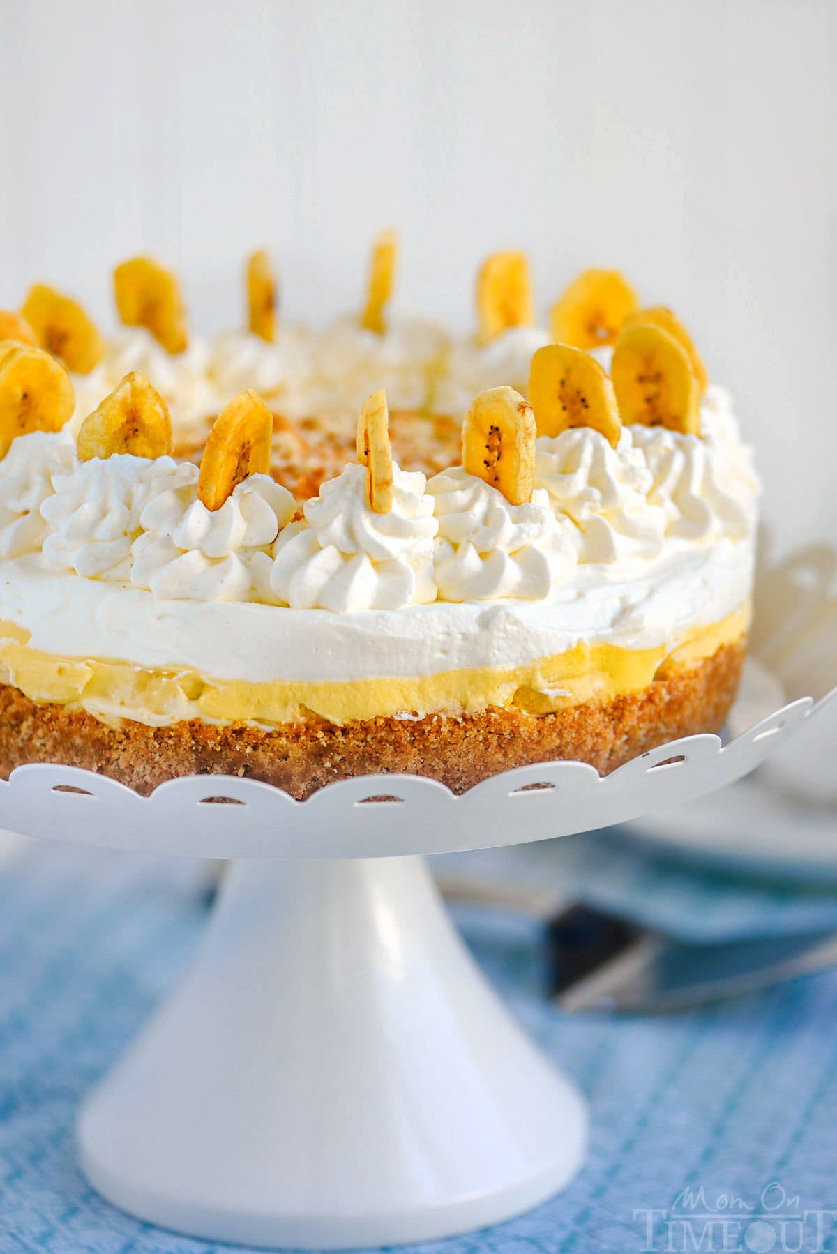 Whole no bake banana pudding cheesecake on white metal stand ready to be served.