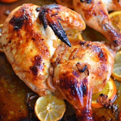 top down look at half a chicken roasted with a lemon and orange glaze sitting on a sheet pan.