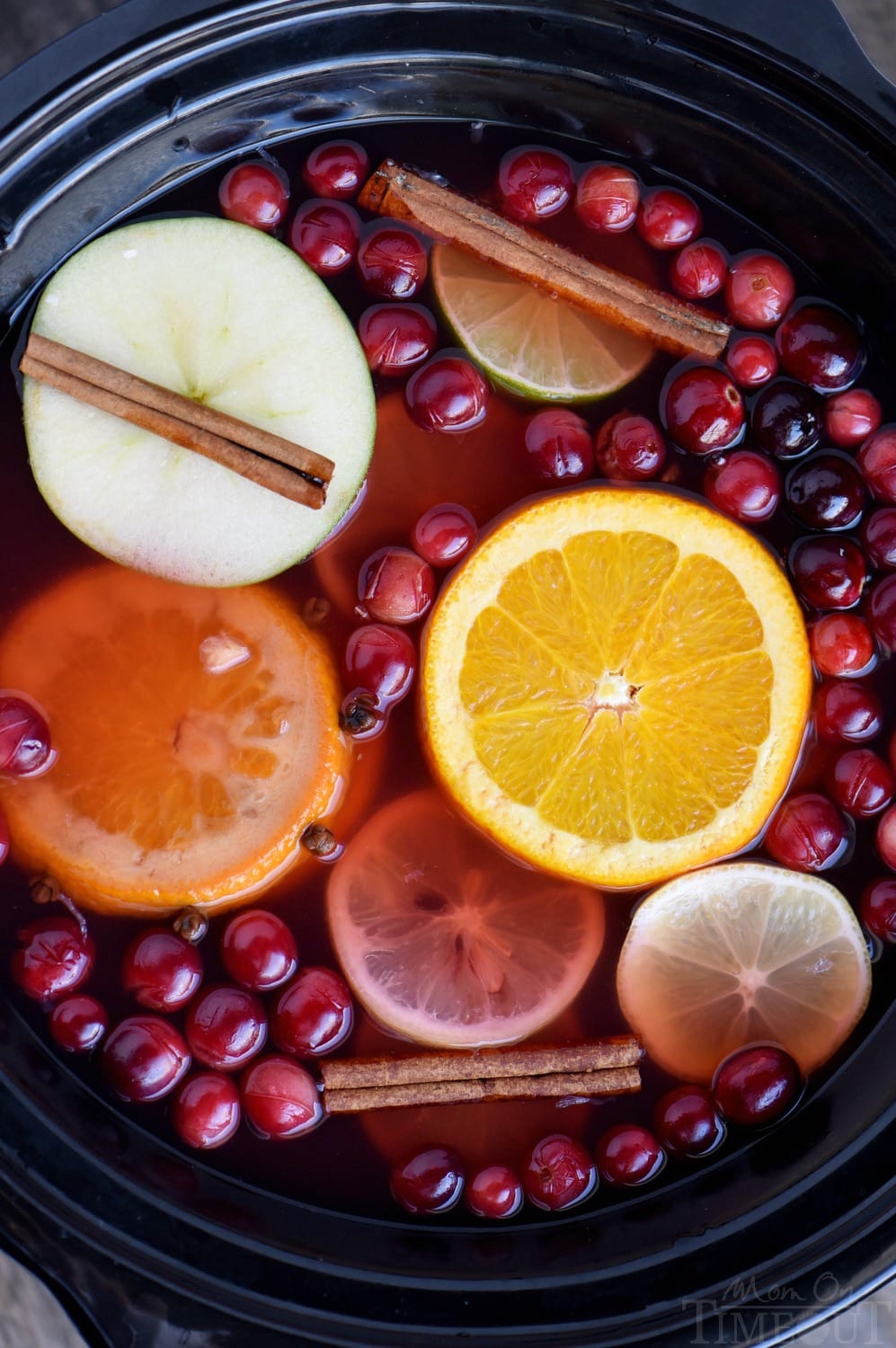 top down view crockpot full of cranberry cider with apple and orange slices and cinnamon sticks and cranberries floating on top