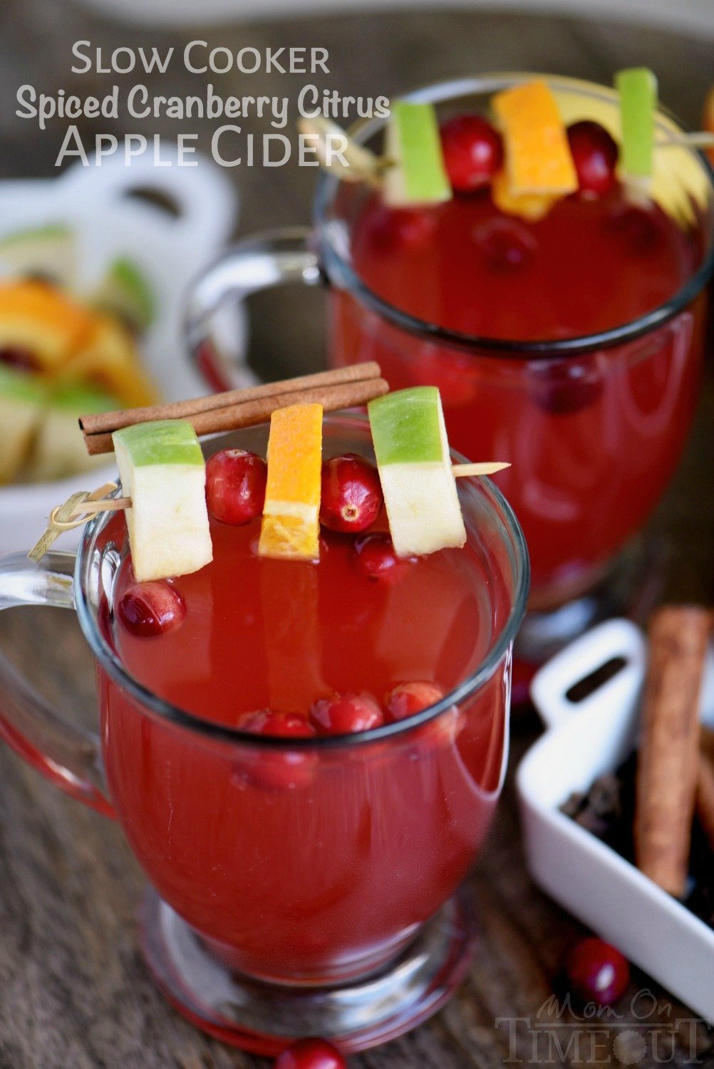 two glass mugs with cranberry apple cider on wood board with apple cranberry orange garnish