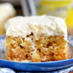 Piece of pineapple cake recipe on blue and white plate topped with pineapple fluff frosting.