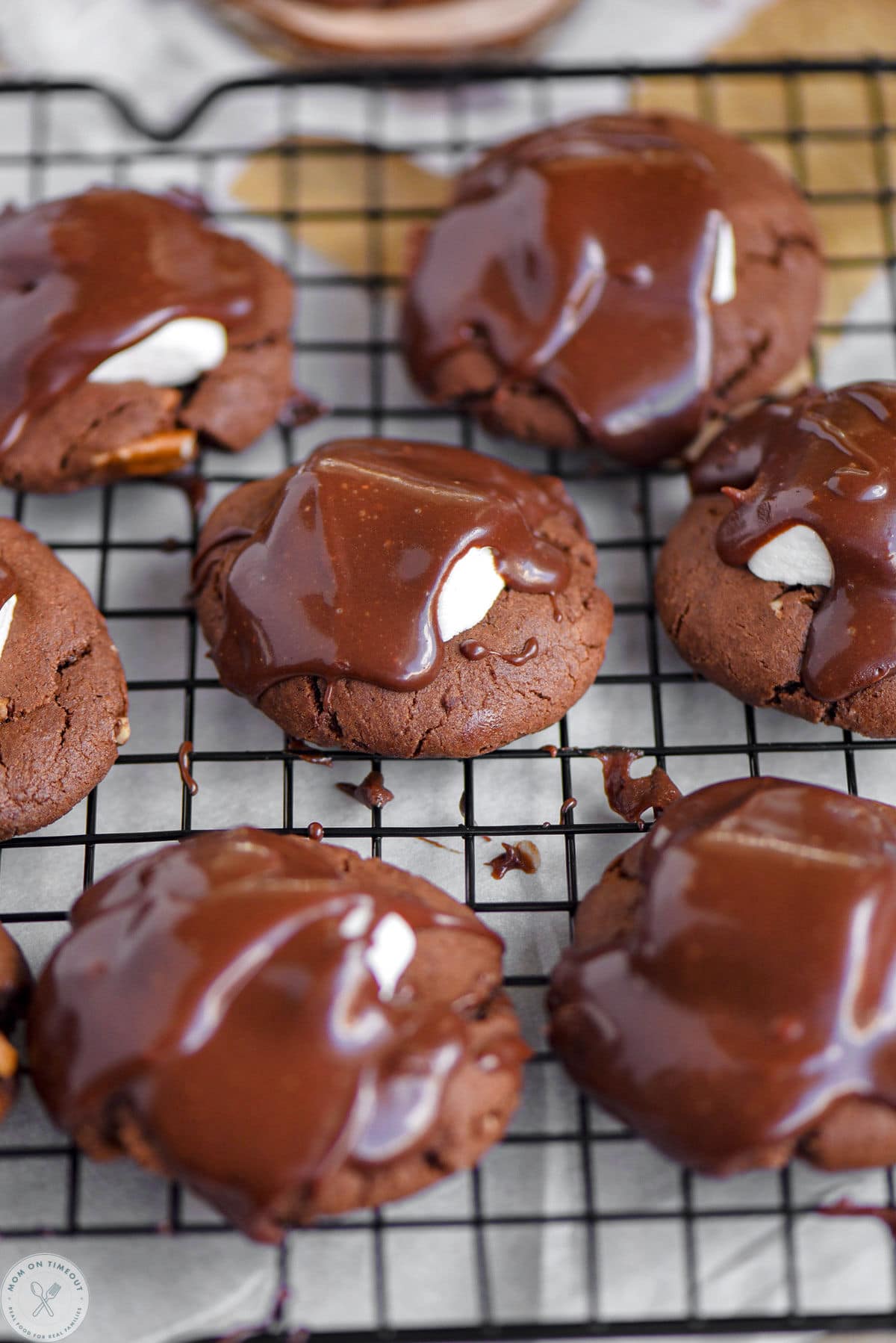 A cooling rack topped with chocolate marshmallow cookies with the glaze setting up.