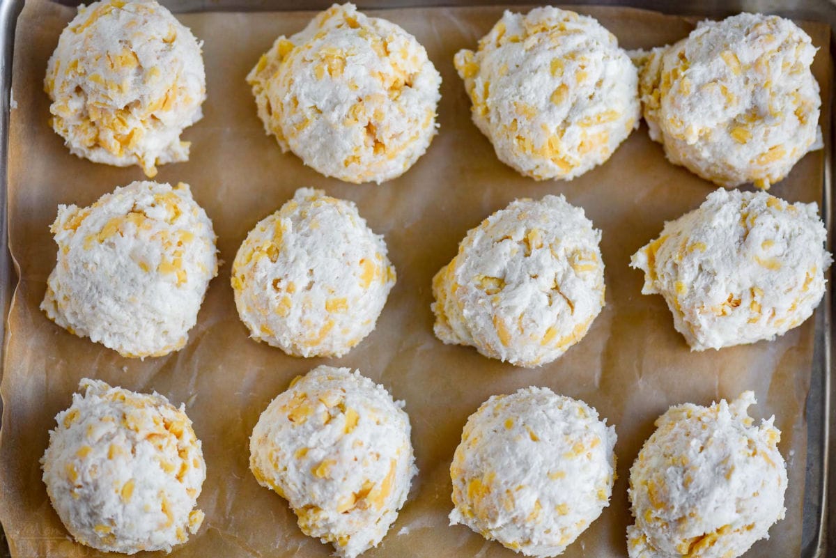 cheesy biscuits on brown parchment paper on baking sheet ready to go in the oven.