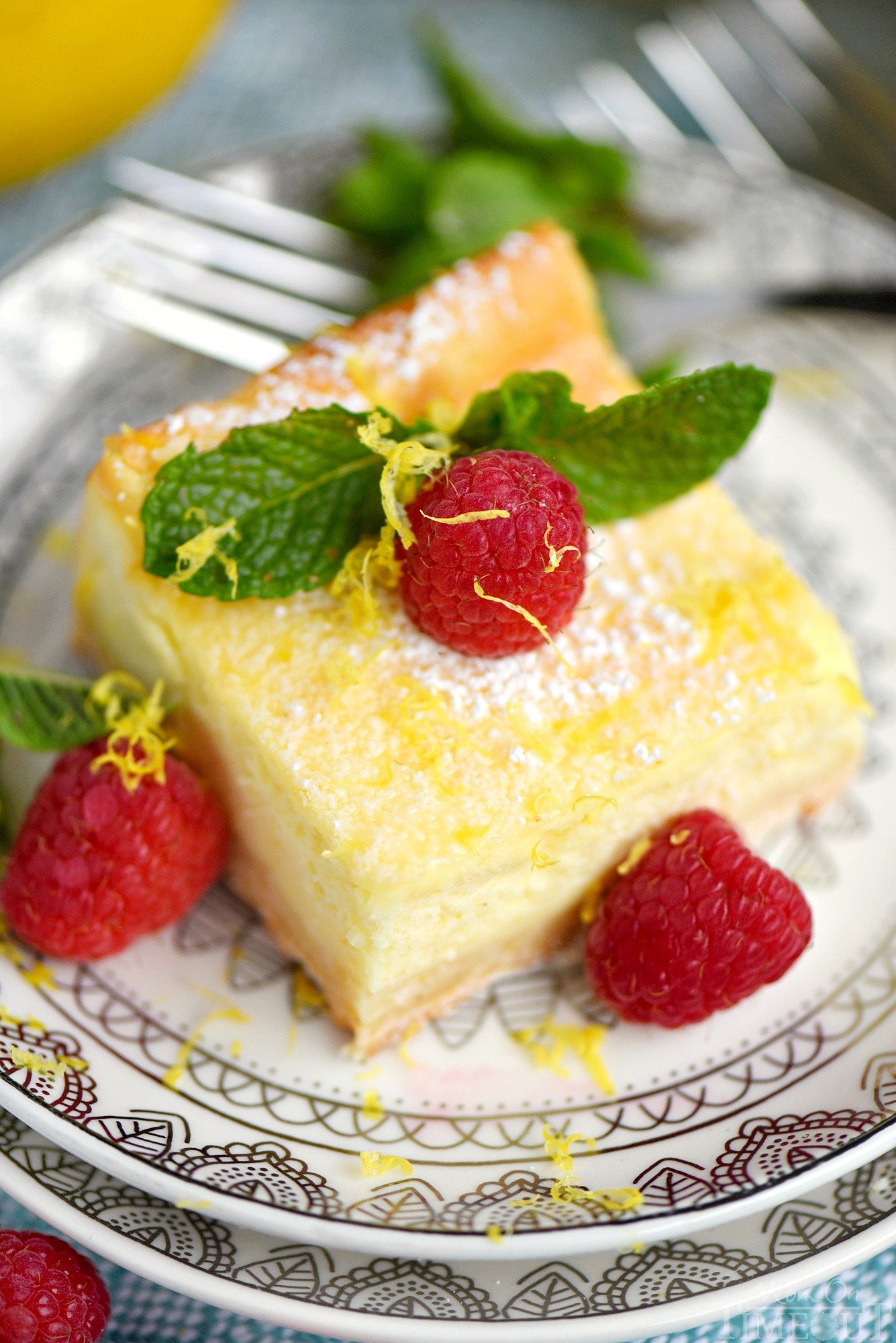 My Aunt Pam's Lemon Cheesecake Bars are made with lots of fresh lemon juice and zest so they're bursting with lemon flavor! Extra creamy, super easy and always a crowd pleaser! Top with powdered sugar, fresh raspberries, and extra lemon zest for a pretty presentation! // Mom On Timeout
