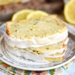 two slices of lemon zucchini loaf cake stacked on each other on small white plate. cake has a a lemon glaze on the top.