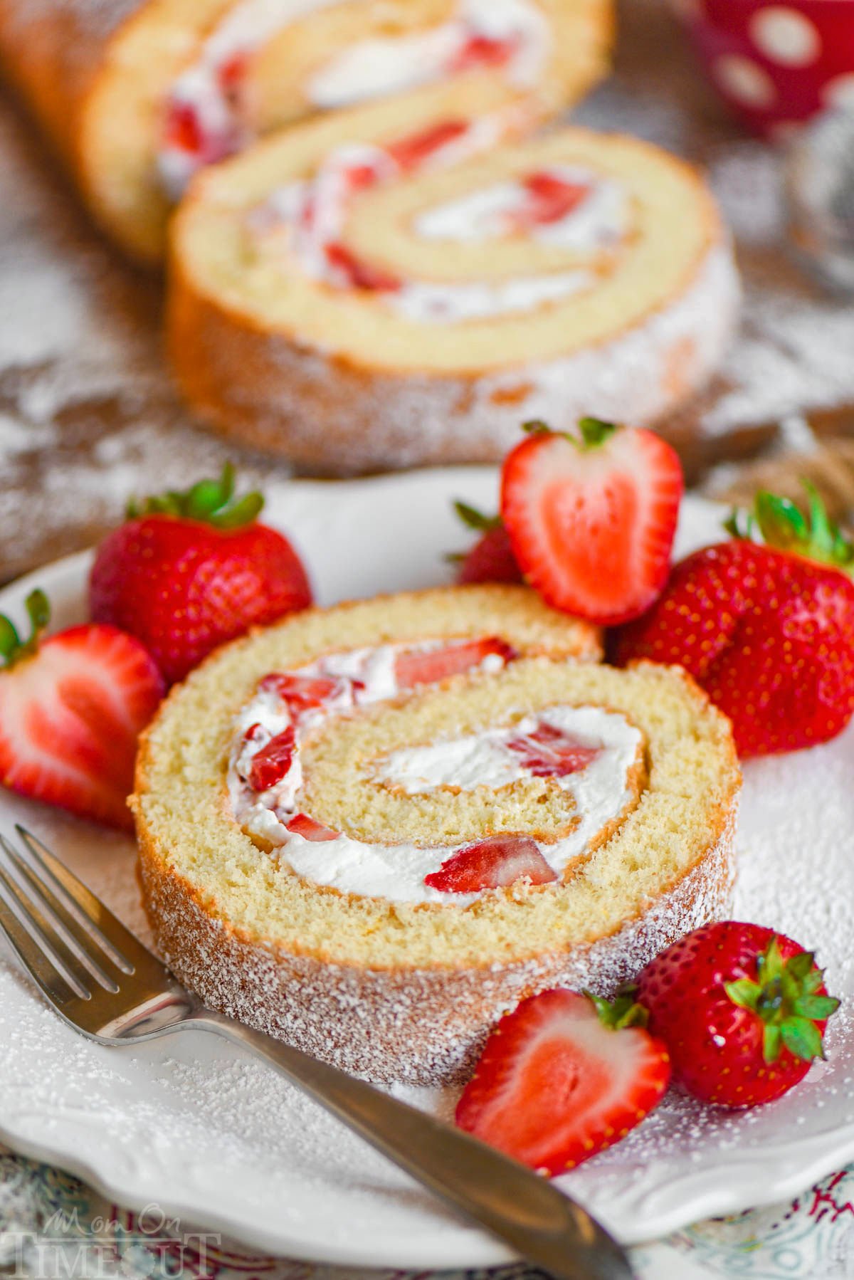 Slice of strawberry cake roll on white plate with fresh strawberries.