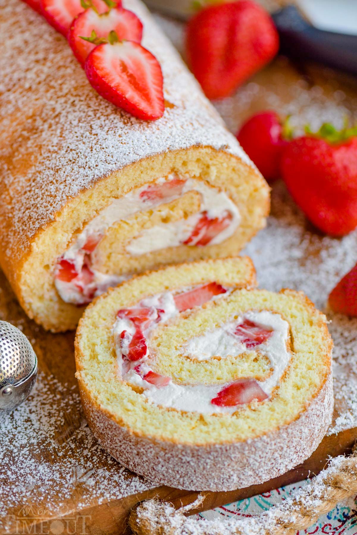 Close up view of strawberry shortcake roulade with one slice of cake cut off. Fresh strawberries on top of cake.