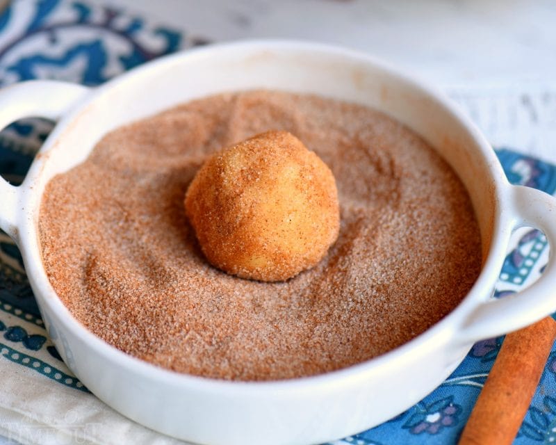 snickerdoodle cookie dough ball being rolled in cinnamon sugar mixture