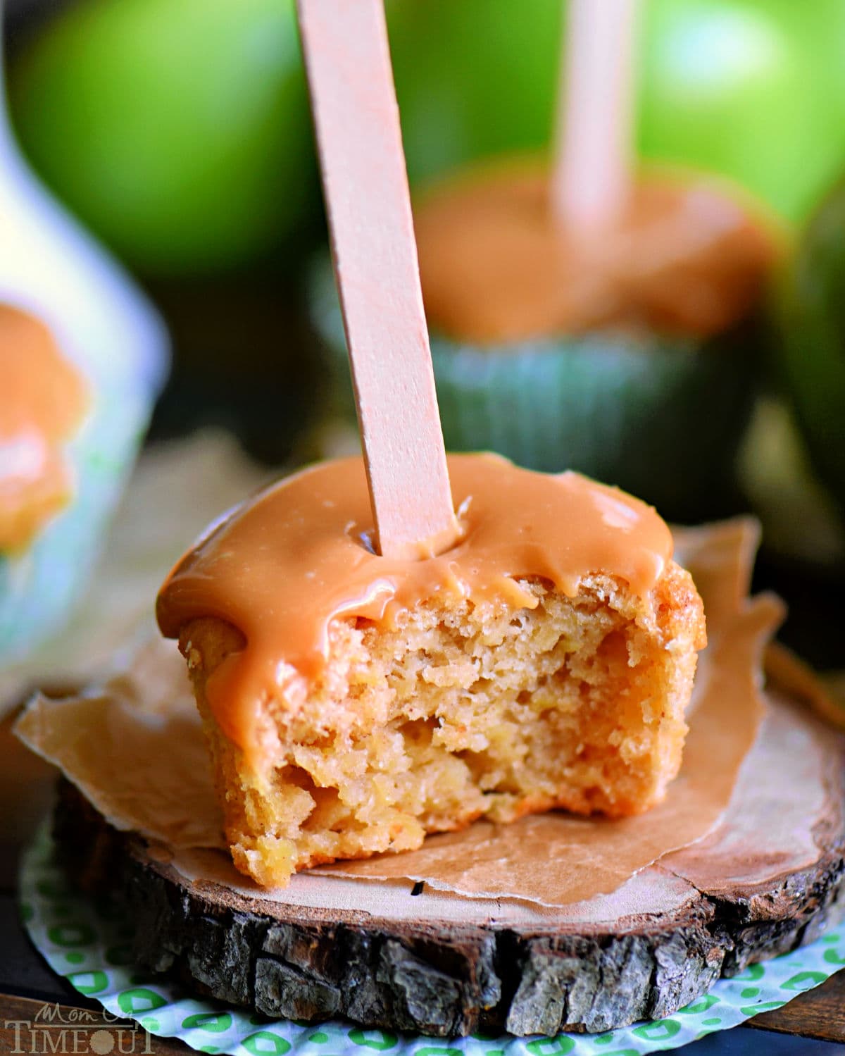 Cupcake alla mela caramellata seduto su un piccolo sottobicchiere di legno con un morso preso da esso.