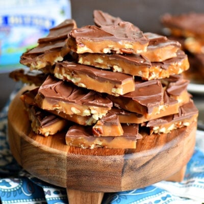 broken up toffee topped with chocolate sitting on a small round wood serving board.