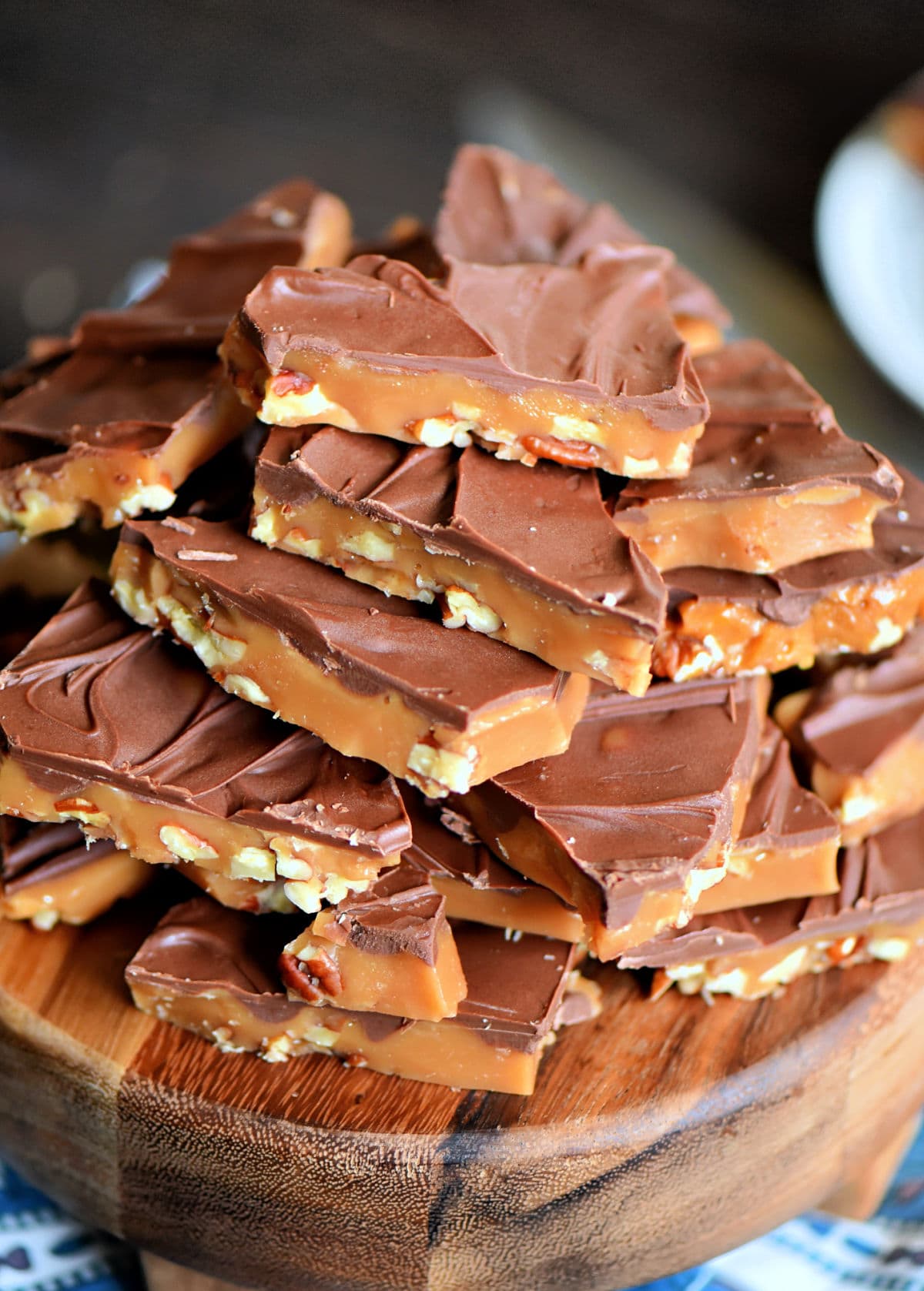 angled look at giant stack of toffee topped with milk chocolate sitting on a round wood board ready to be enjoyed.