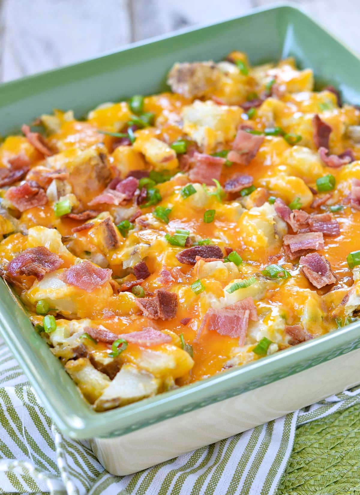 potato casserole made with bacon, cheese and green onions in a square 9 inch casserole dish with a green interior. 