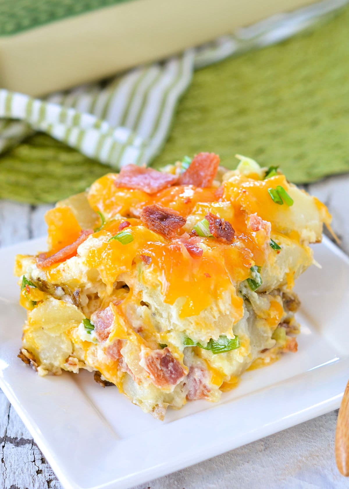 a generous serving of twice baked potato casserole sitting on a small white square plate with casserole dish in back ground.