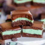 three mint brownies stacked in a pyramid. top brownie has bite taken out of it. more brownies can be seen in the background.