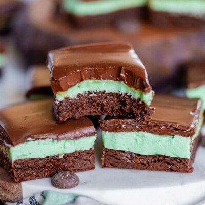 three mint brownies stacked in a pyramid. top brownie has bite taken out of it. more brownies can be seen in the background.
