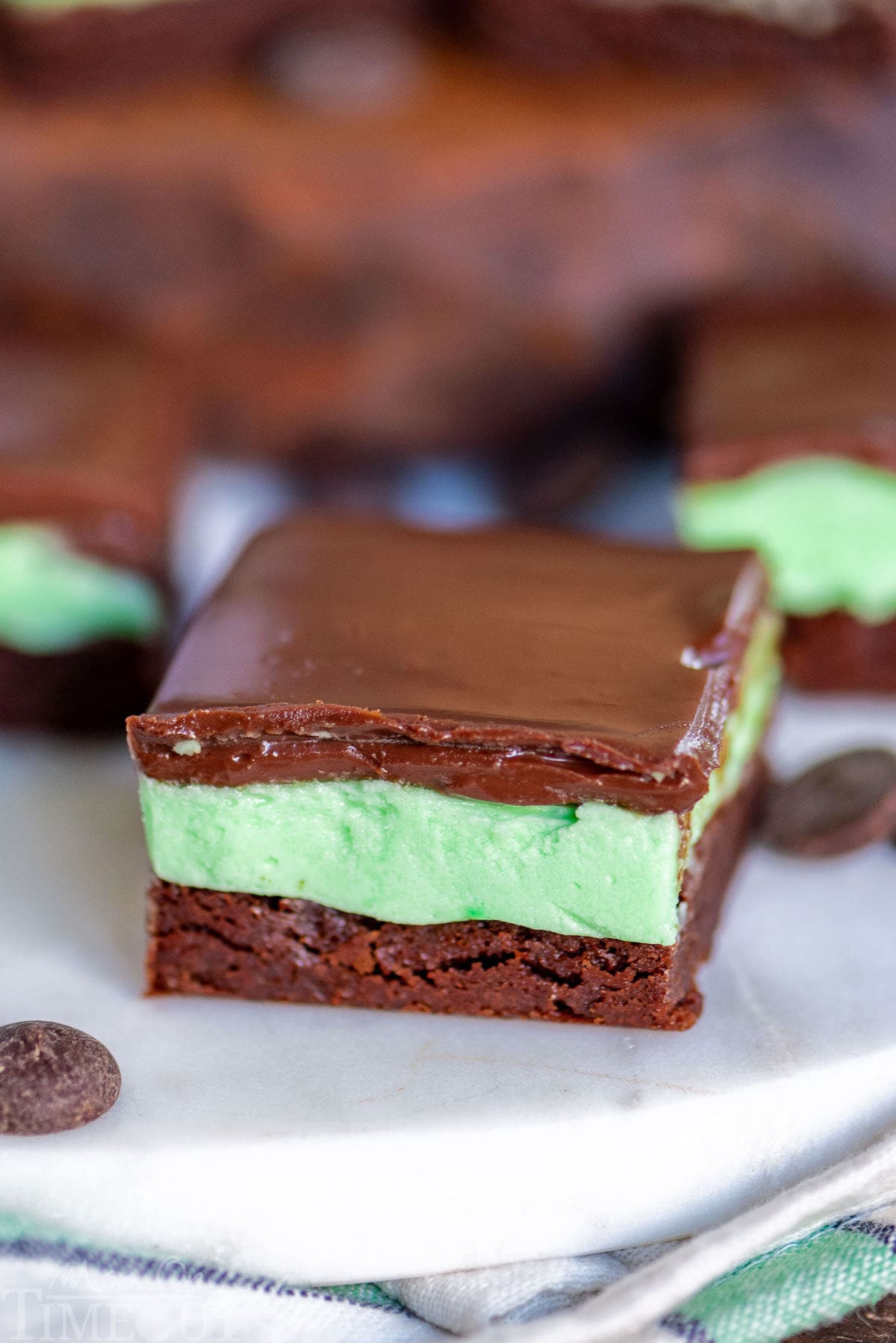 single chocolate mint brownie sitting on marble surface. more brownies can be seen behind it.