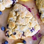 top down view of lemon blueberry scone on a piece of brown parchment paper with fresh blueberries scattered about.