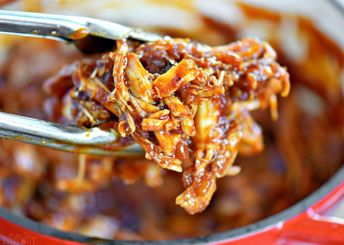 bbq pulled chicken held above the saucepan with tongs.