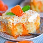 slice of creamsicle cake on round white plate topped with fluff frosting and orange candy.