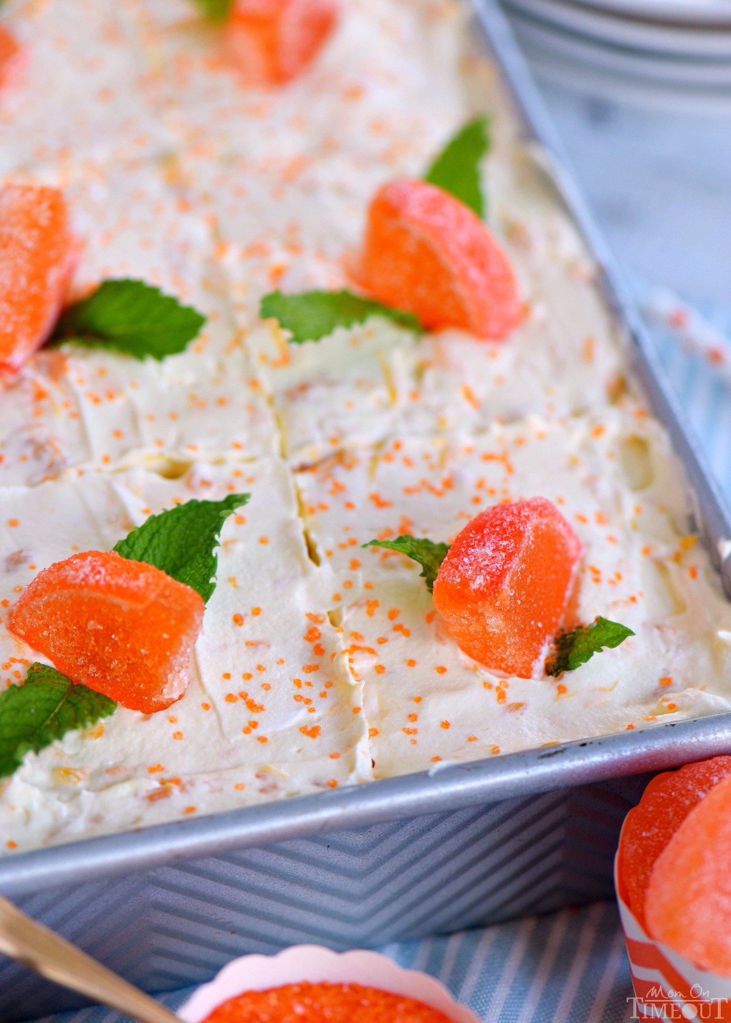 whole creamsicle cake in a 9 by 13 metal baking dish garnished with candy oranges and mint leaves
