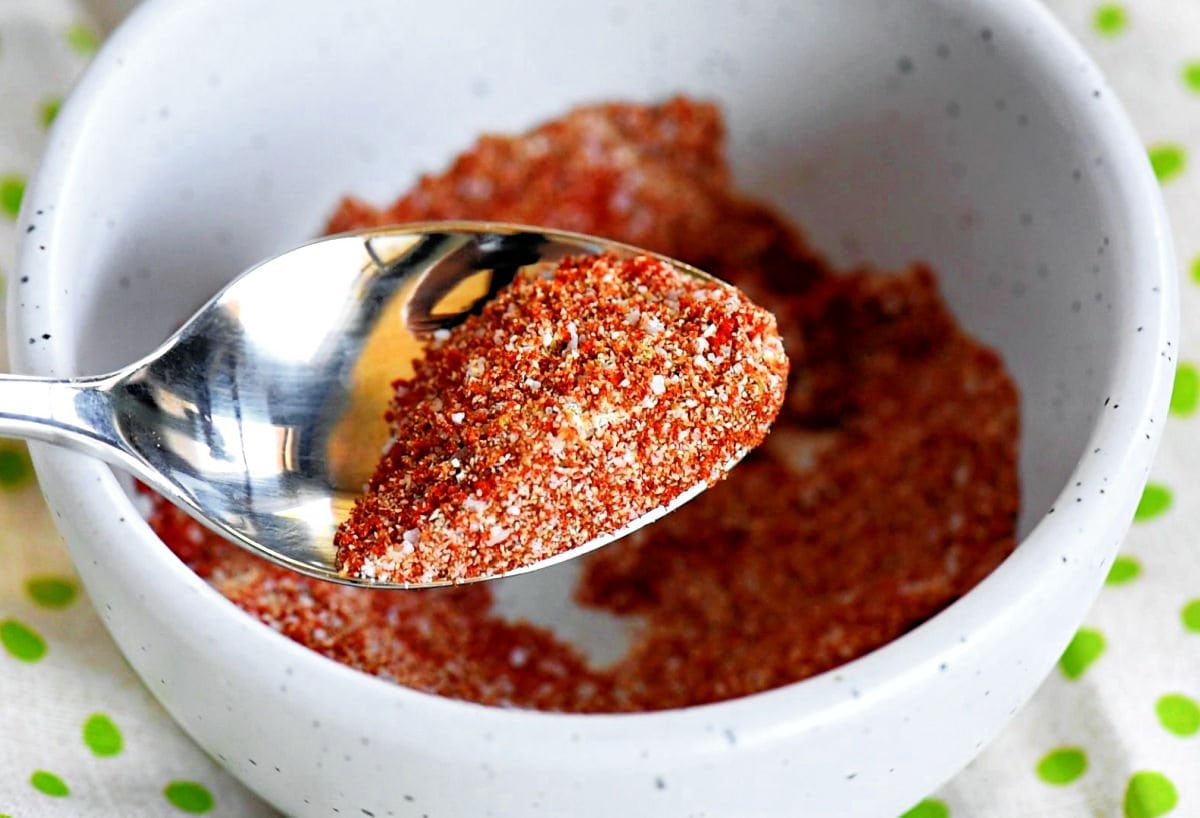 small bowl with a seasoning blend mixed together ready to be rubbed on the chicken thighs. spoon with some of the seasoning is held above the bowl.